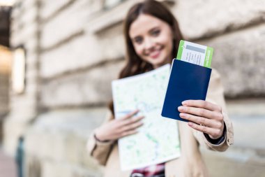 Gülen, harita tutan ve pasaportu uçak biletiyle gösteren kadınların seçici odak noktası.