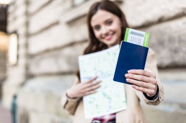 Selective focus of woman smiling, holding map and showing passport with air ticket clipart