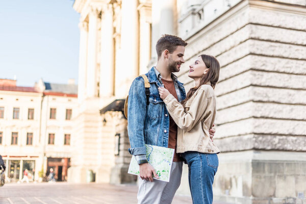 Selective focus of happy couple hugging and looking at each other with map in city