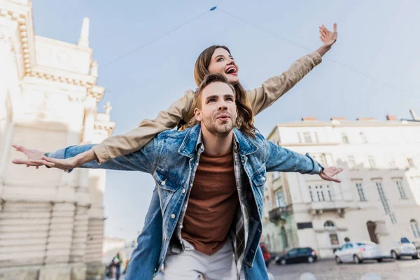 Nízký Úhel Pohledu Muže Otevřenými Pažemi Piggybacking Vzrušená Dívka Městě — Stock fotografie