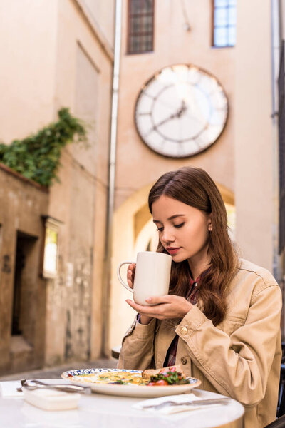 Selective focus of woman holding white cup of tea in cafe in city