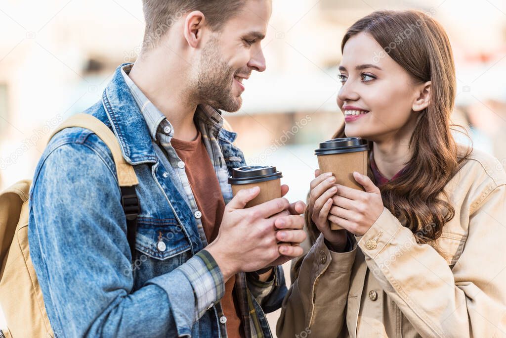 Man and girl holding disposable cups of coffee with clenched hands, looking at each other and smiling 