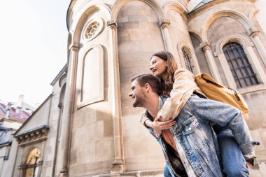 Low angle view of man piggybacking girlfriend near building in city clipart