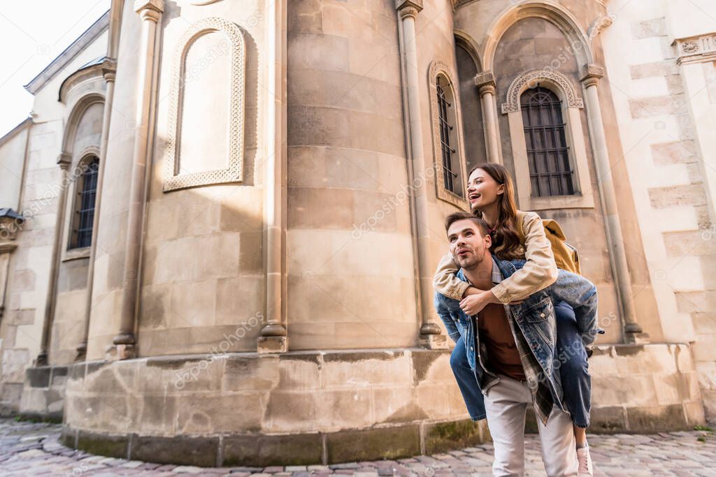 Excited man piggybacking girlfriend near building in city