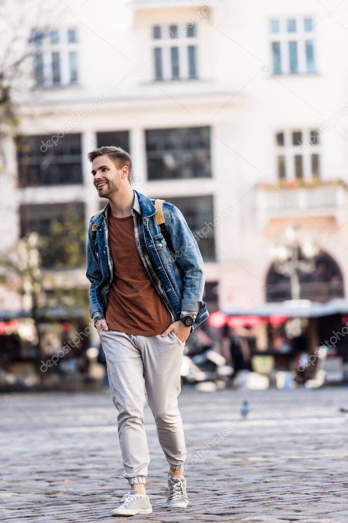 Man with backpack and hands in pockets smiling and walking in city