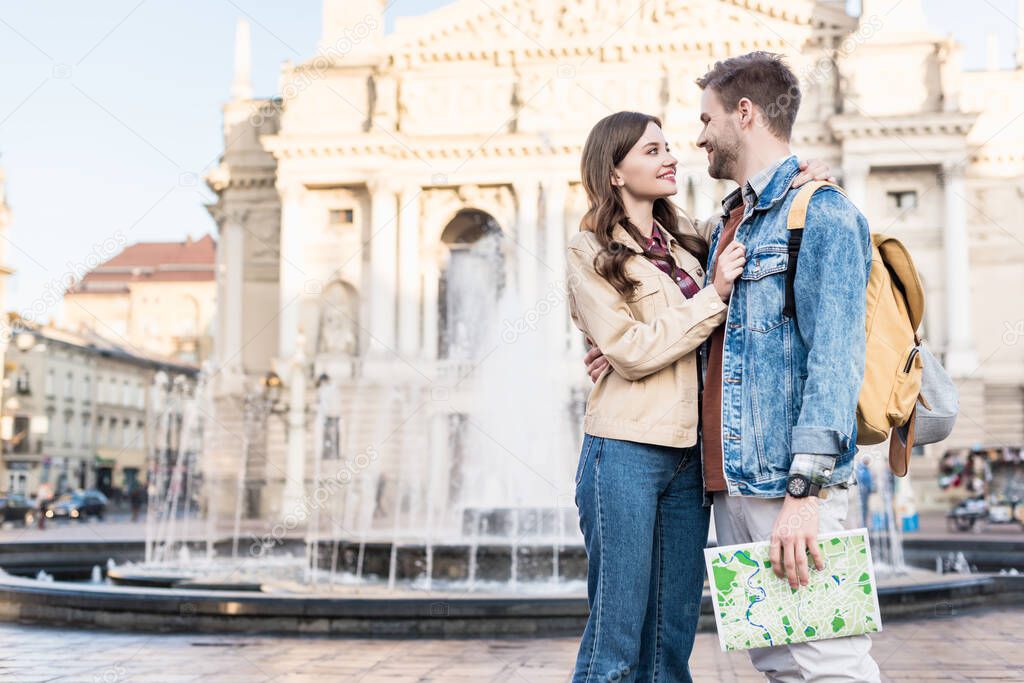 Couple looking at each other hugging with map near fountain in city