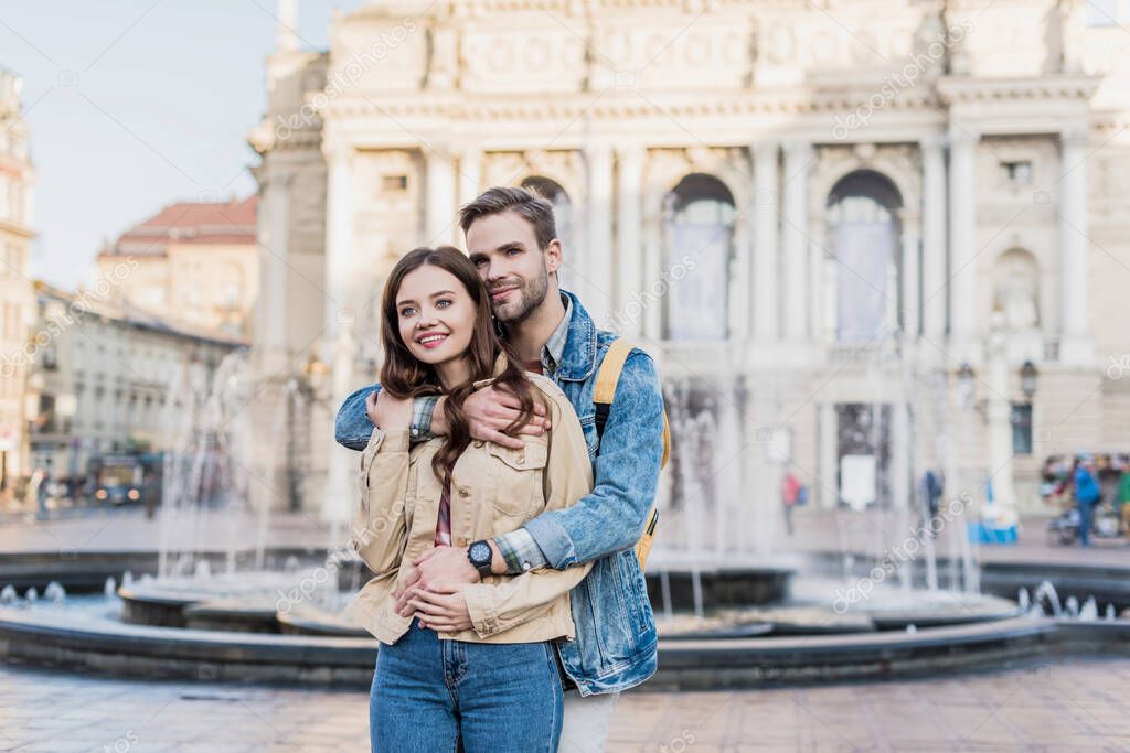 Happy couple hugging and smiling near fountain in city