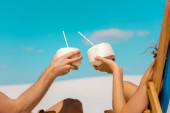 kivágott kilátás fiatal pár ül fedélzeti székek kókuszos italok homokos strandon
