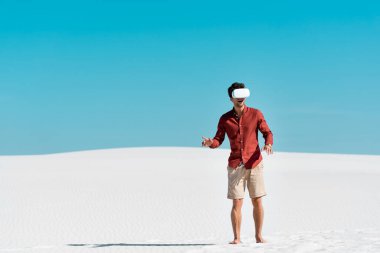 handsome man on sandy beach in vr headset against clear blue sky clipart