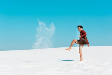Deri çantalı mutlu adam kumsala kum atıyor.