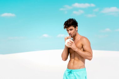 Kumsalda hindistan cevizi içkisi ve mayo giymiş kaslı vücutlu seksi bir adam.