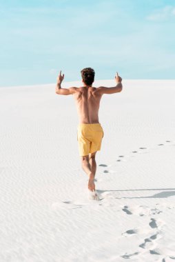 Yüzme şortlu, kaslı gövdesi kumsalda koşan bir adam.