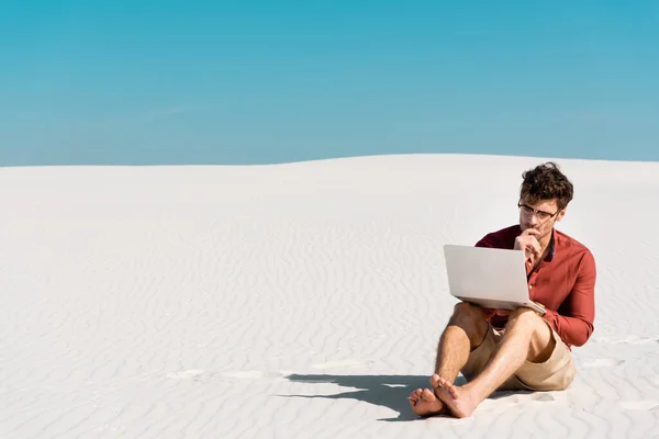 Zamyślony Przystojny Freelancer Piaszczystej Plaży Laptopem Przed Jasnym Błękitnym Niebem — Zdjęcie stockowe
