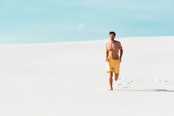 笑顔の男がショートパンツを履いて砂浜を走る筋肉質の胴 — ストック写真