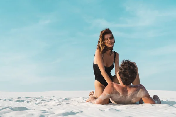 セクシーな若い女性座っています上のボーイフレンド砂のビーチに横たわって — ストック写真
