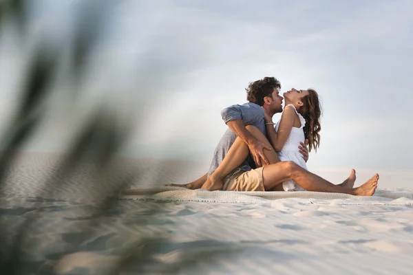 年轻夫妇在沙滩上在毛毯上亲吻的选择性焦点 — 图库照片