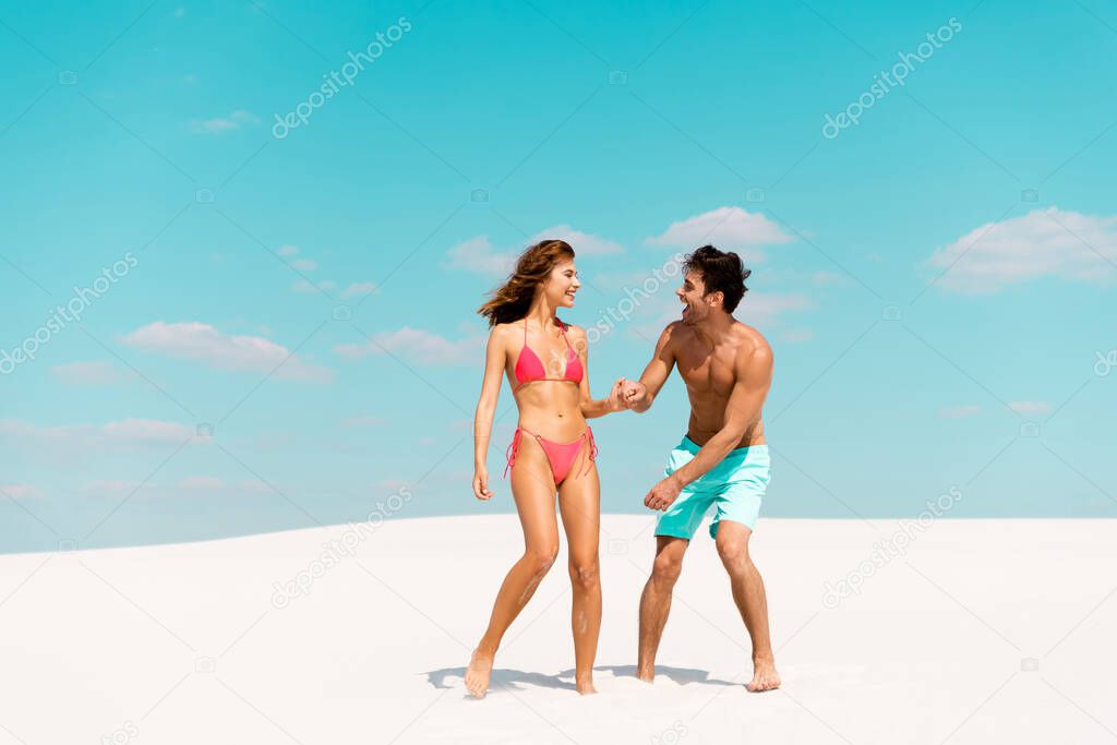 smiling young couple holding hands on sandy beach