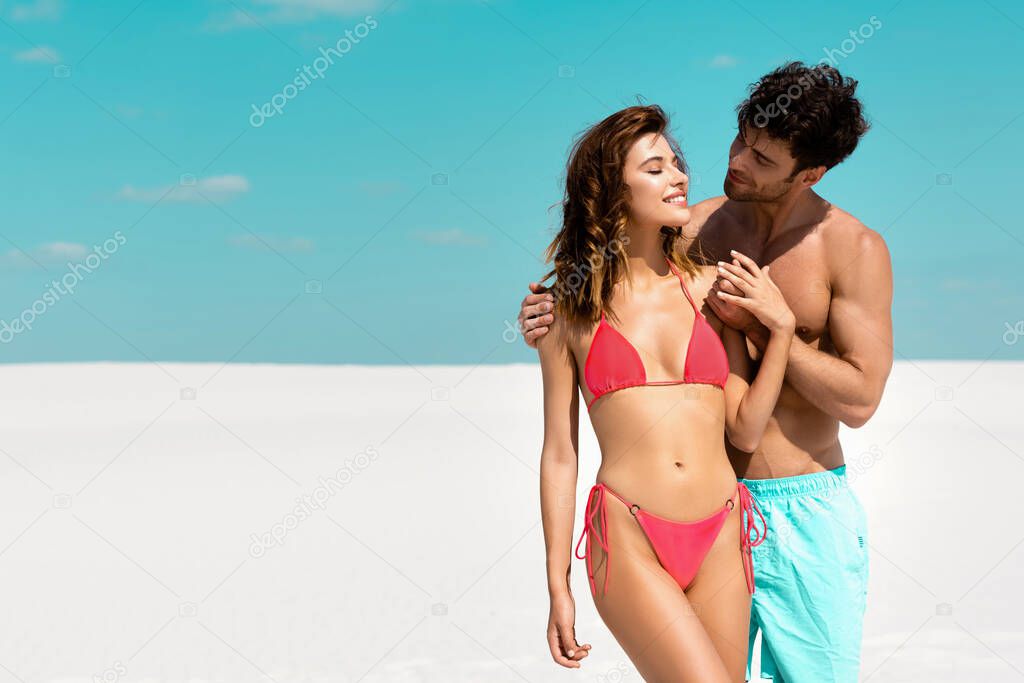 young man embracing beautiful sexy girlfriend on sandy beach