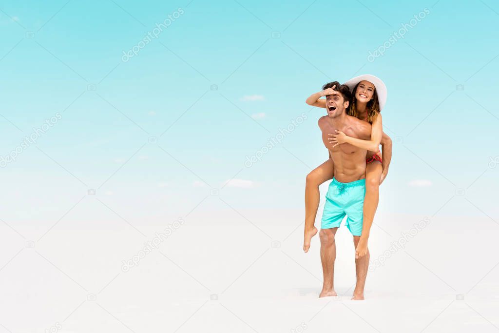 smiling young man piggybacking girlfriend on sandy beach