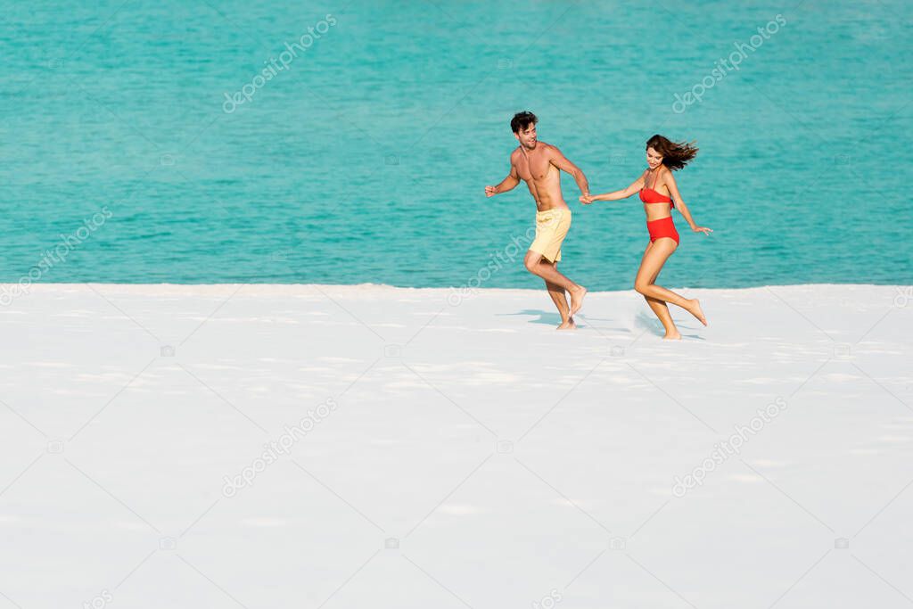 young sexy couple running on sandy beach near ocean