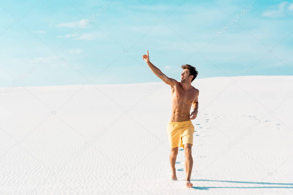 man in swim shorts with muscular torso walking on sandy beach
