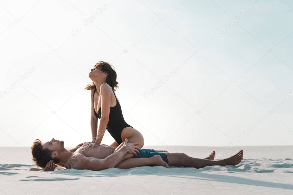 side view of sexy passionate young couple lying on sandy beach 