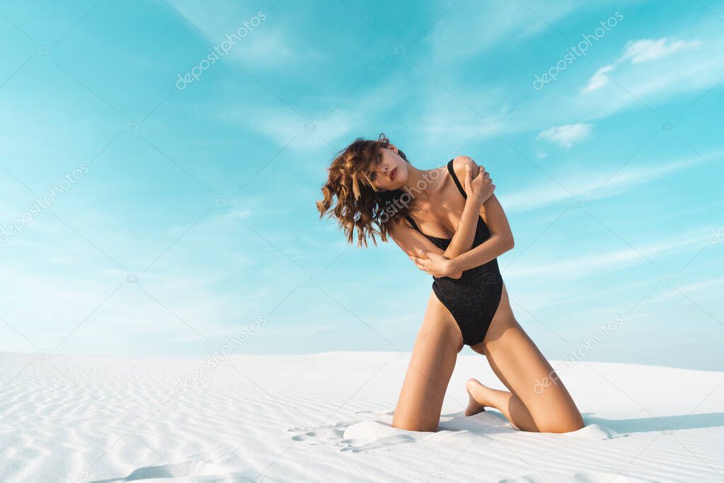 sexy beautiful woman in black swimsuit posing on sandy beach with blue sky