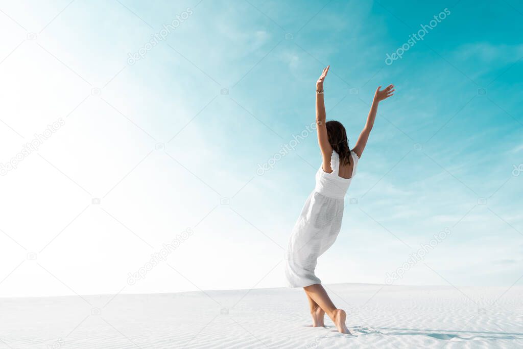 beautiful girl in white dress with hands in air on sandy beach with blue sky