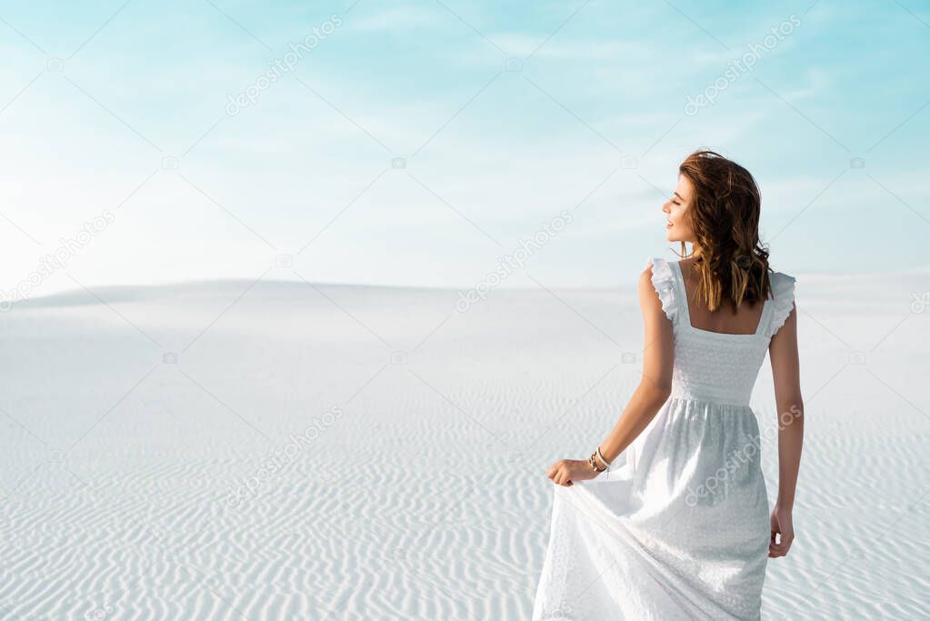back view of beautiful girl in white dress on sandy beach with blue sky