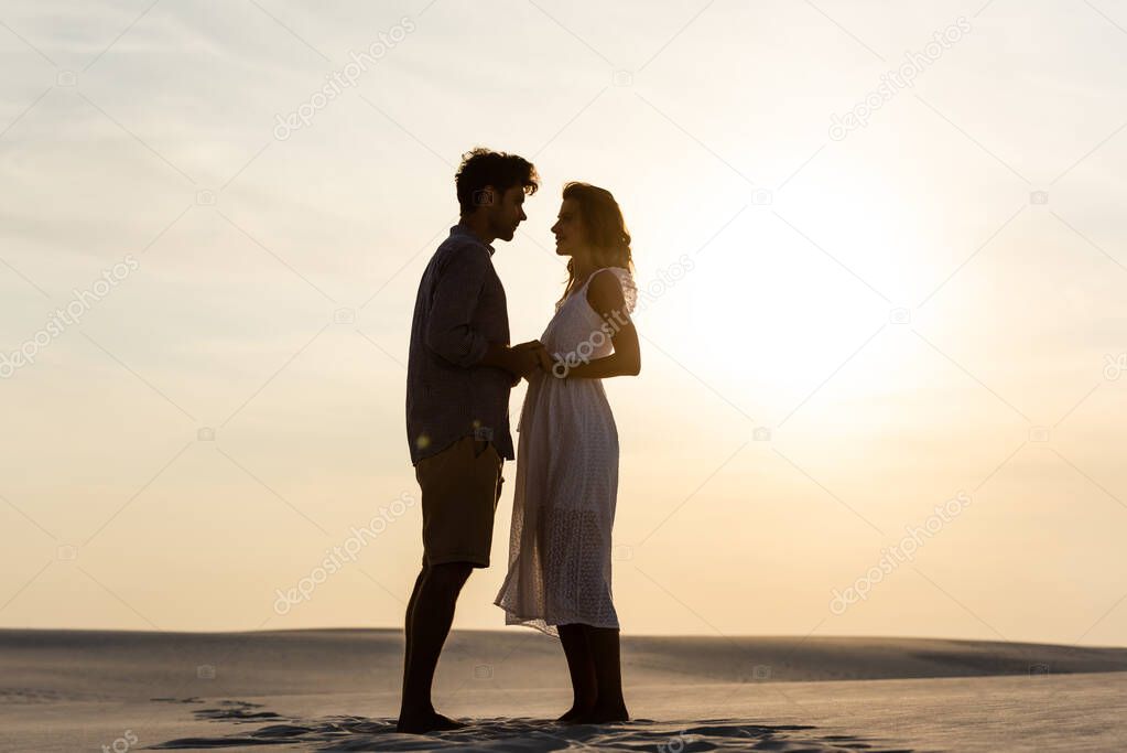 side view of young couple holding hands on sandy beach at sunset