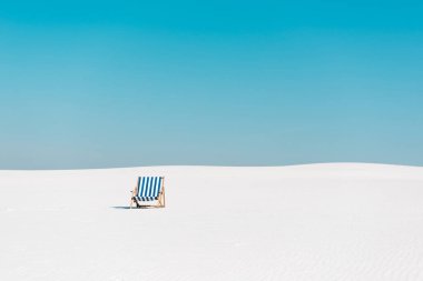 empty deck chair on sandy beach against clear blue sky clipart
