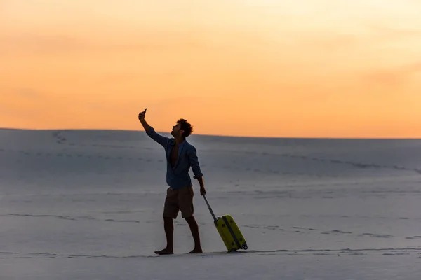 Gün Batımında Kumsalda Seyahat Çantası Akıllı Telefonuyla Yürüyen Bir Adamın — Stok fotoğraf