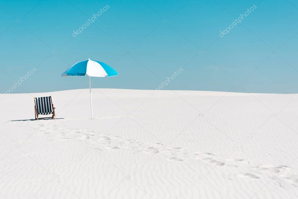 deck chair and umbrella on sandy beach with traces against clear blue sky
