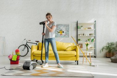 çekici genç bir kadın oturma odasında elektrikli süpürge tutuyor. 