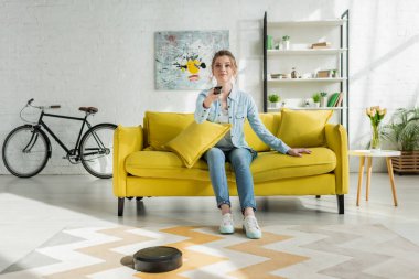 çekici bir kadın TV izlerken robotik elektrikli süpürge oturma odasında halı yıkıyor. 