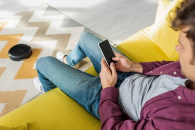 Oturma odasında halı yıkarken akıllı telefonu boş ekranla tutan adamın seçici odak noktası.