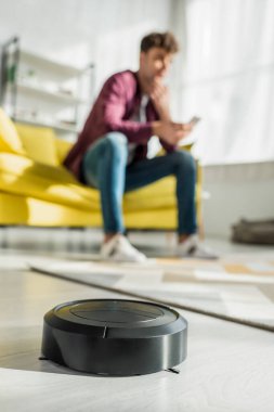 Oturma odasındaki adamın yanında halı yıkayan robot elektrik süpürgesinin seçici odağı.