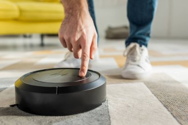 Oturma odasındaki robot elektrik süpürgesini işaret eden adamın kırpılmış görüntüsü