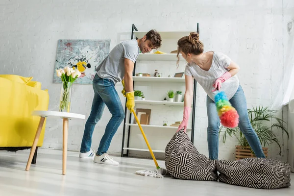 Frau Hält Bohnensackstuhl Während Mann Boden Mit Wischmopp Reinigt — Stockfoto