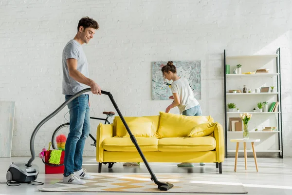 Glücklicher Mann Benutzt Staubsauger Neben Frau Wohnzimmer — Stockfoto