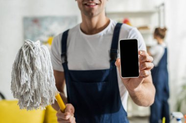 Kesilmiş mutlu temizlikçi görüntüsü boş ekran ve paspasla akıllı telefon tutuyor 