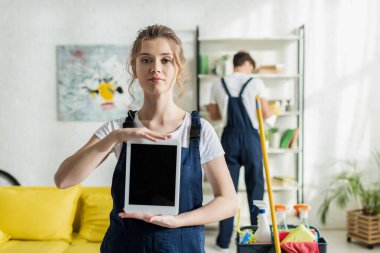 Boş ekranlı dijital tableti tutan mutlu ve çekici temizleyicinin seçici odağı 