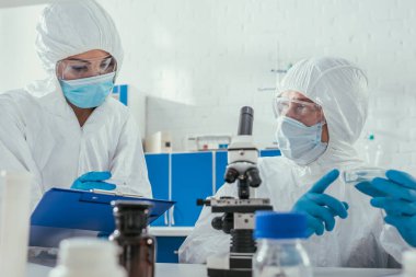 Mikroskop ve tıbbi konteynırların yanında petri kabı tutan iki biyokimyacının seçici odağı