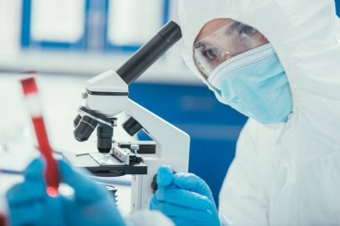 Mikroskop yakınındaki biyokimyagerin seçici odak noktası kan örneğiyle test tüpüne bakmak. 