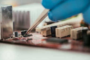 cropped view of engineer testing computer motherboard with tweezers clipart