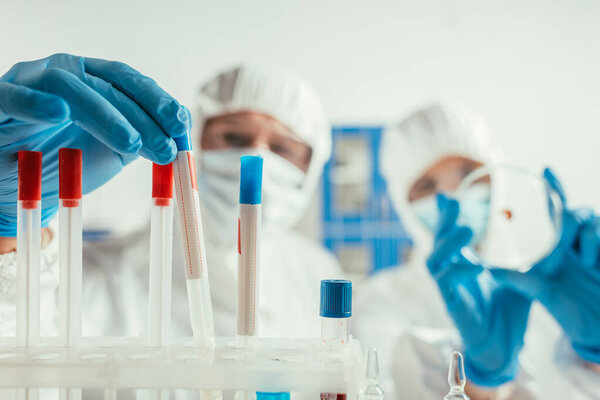 selective focus of biochemist taking test tube near colleague holding petri dish