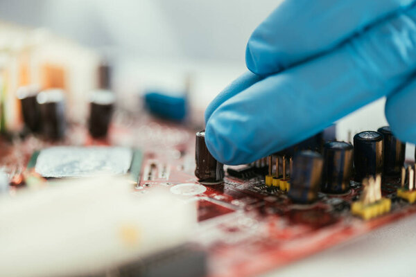 селективная фокусировка руки инженера в резиновой перчатке возле материнской платы компьютера
