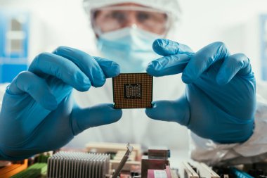 selective focus of engineer holding microchip near computer motherboard clipart