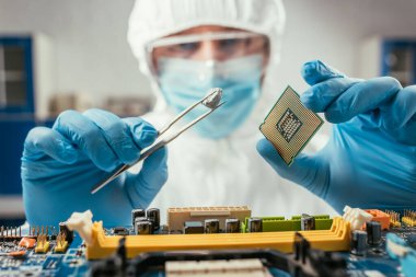 selective focus of engineer holding small stone with tweezers and microchip near computer motherboard clipart