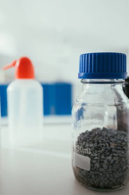 selective focus of glass jar with gravel near plastic container on desk in laboratory clipart